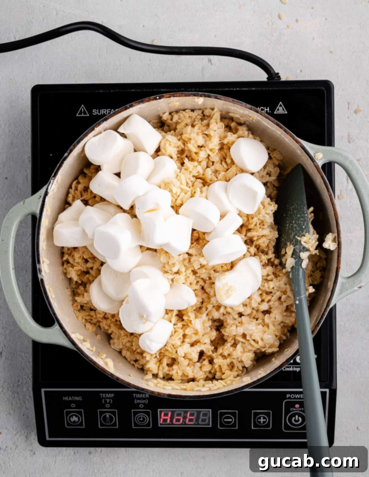 A dutch oven with the sticky rice crispy mixture and large marshmallow halves on top, ready to be mixed in.