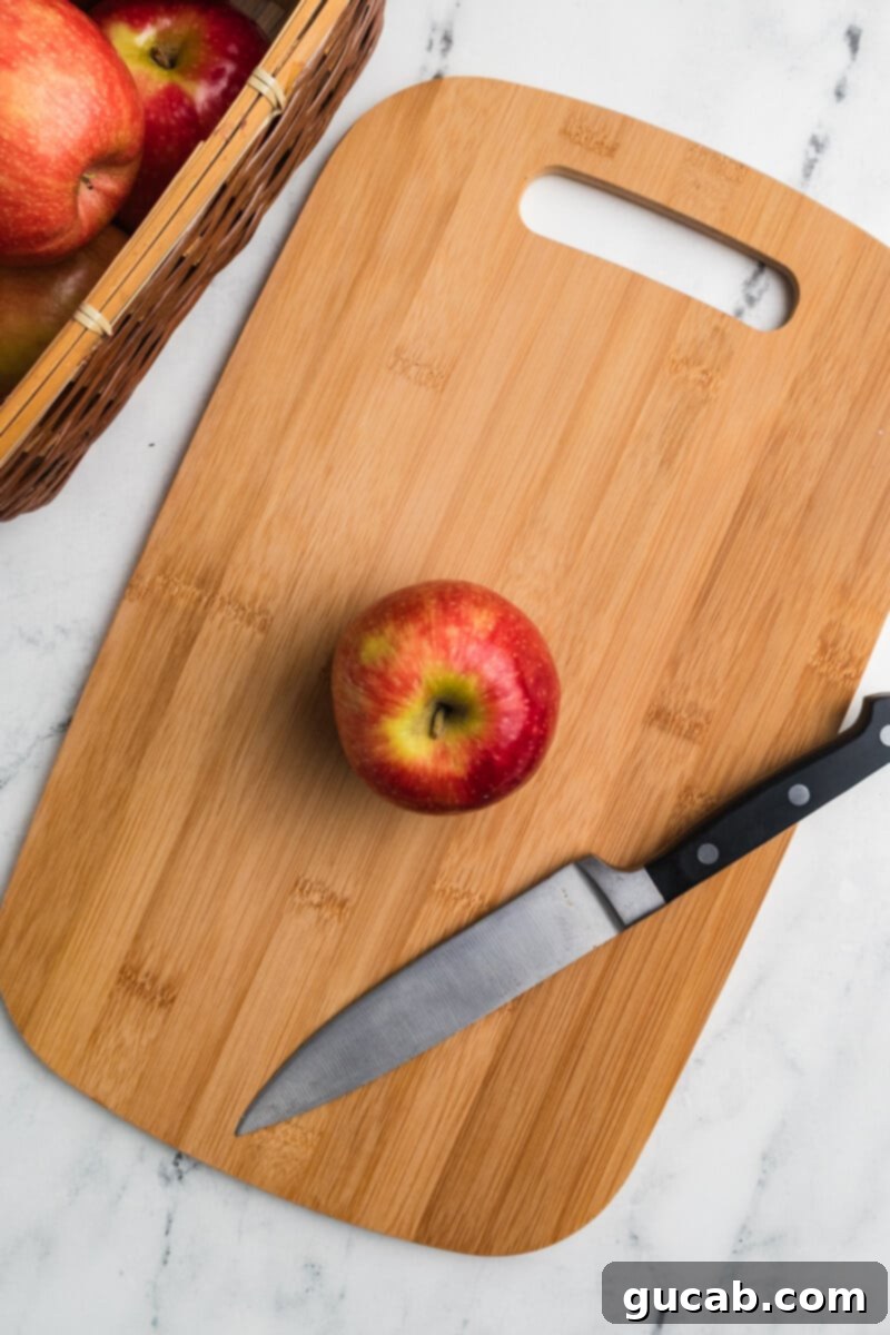 A whole apple resting on a wooden cutting board, ready for preparation.