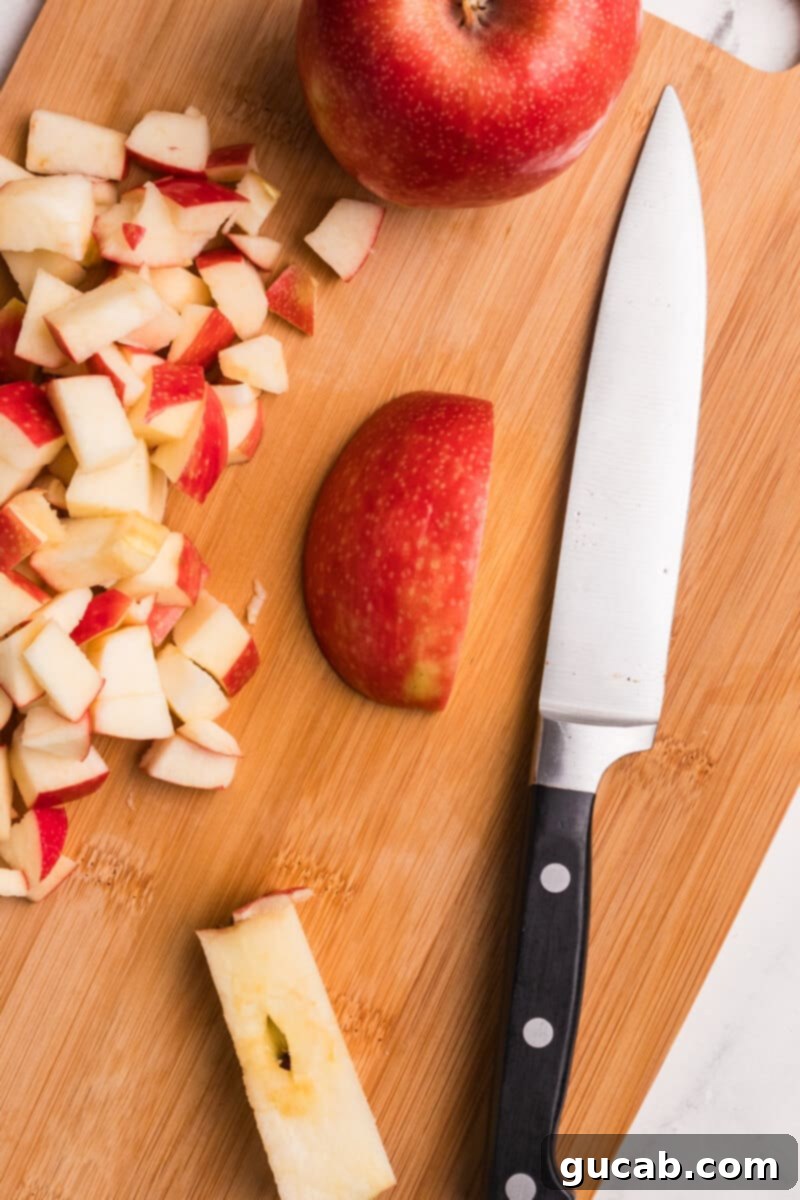 Sliced apple halves and roughly chopped apple chunks scattered on a cutting board, alongside a chef's knife.