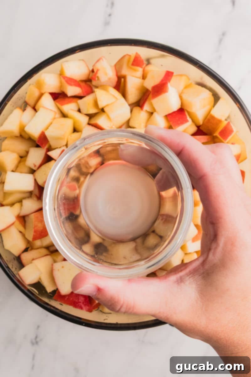 A hand pouring fresh lemon juice from a small bowl over chopped apples in a large Dutch oven.