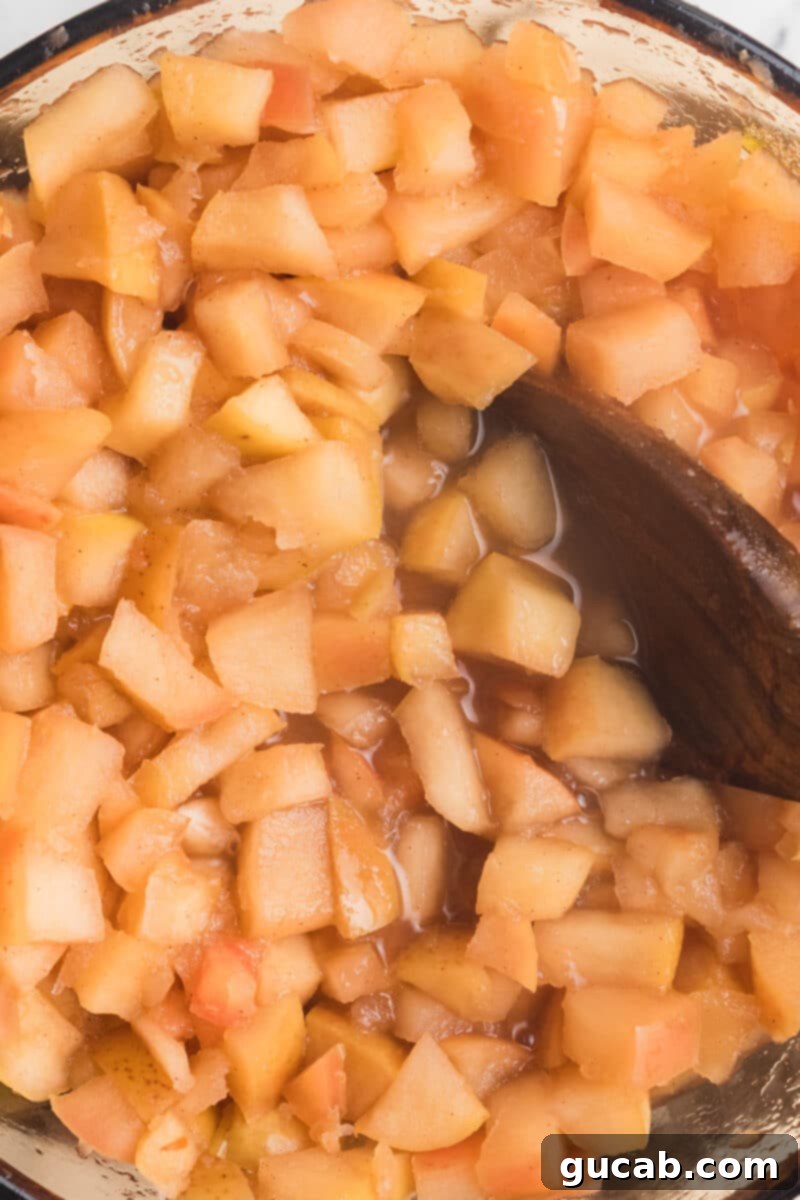 A large wooden spoon stirring soft, cooked apples in a pot, demonstrating their tender consistency.