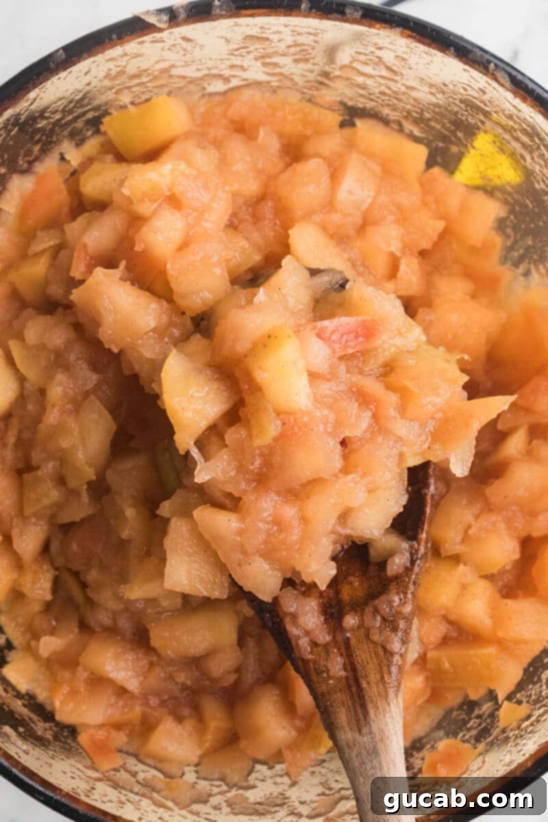 A spoonful of very soft, cooked apples held above the pot, showing their almost disintegrated state.