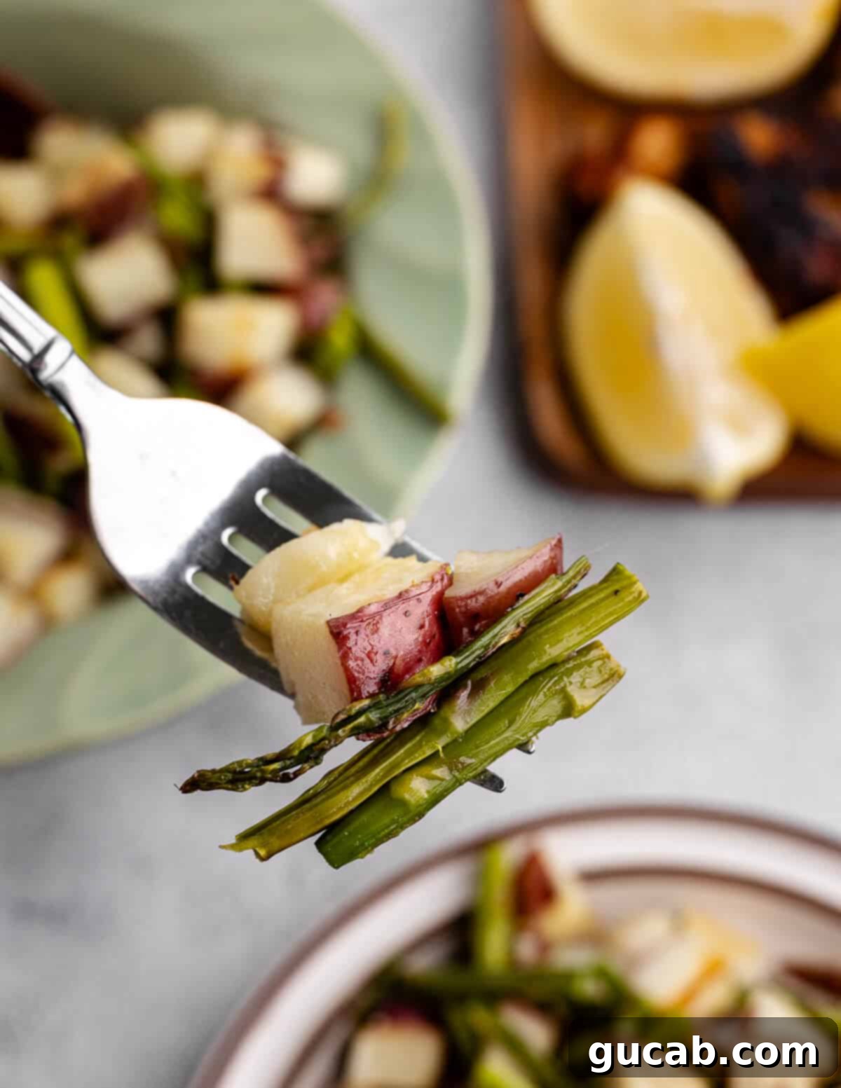 A close-up of a fork holding a single piece of roasted potato and an asparagus spear, showcasing the golden crispiness and tender texture.