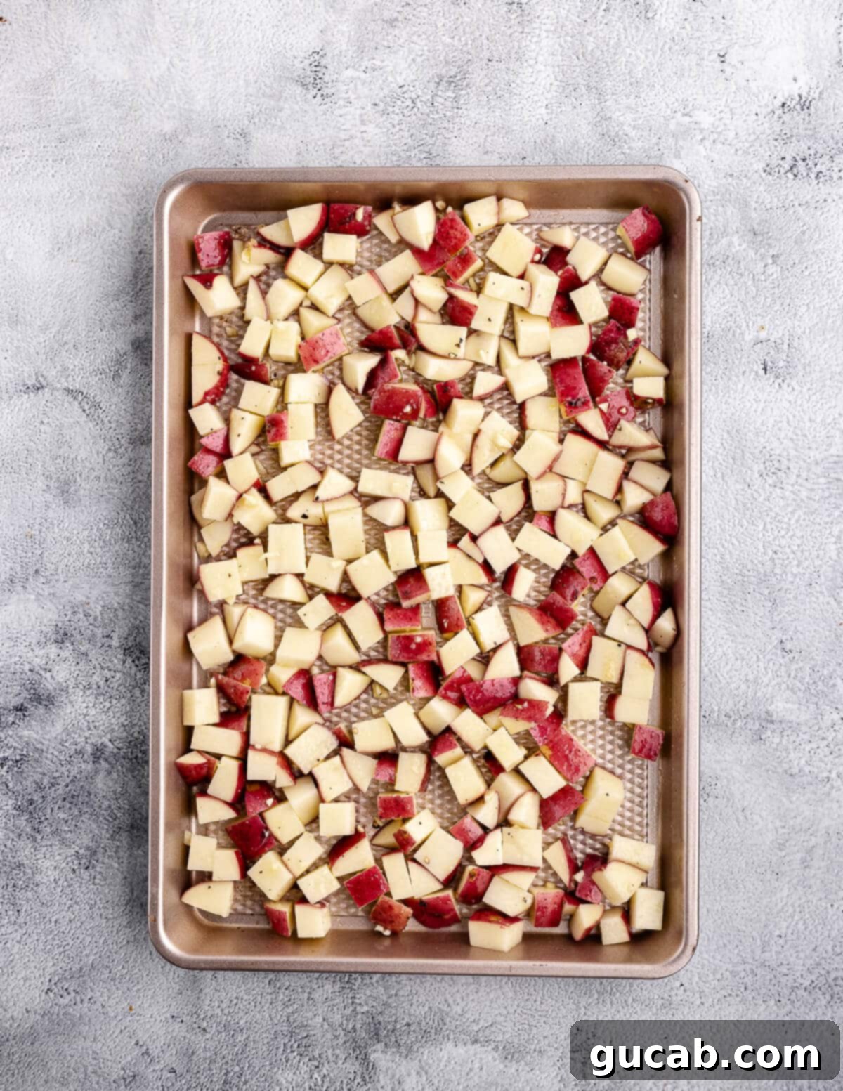 Diced and seasoned red potatoes spread in a single layer on a parchment-lined baking sheet, ready for the oven.
