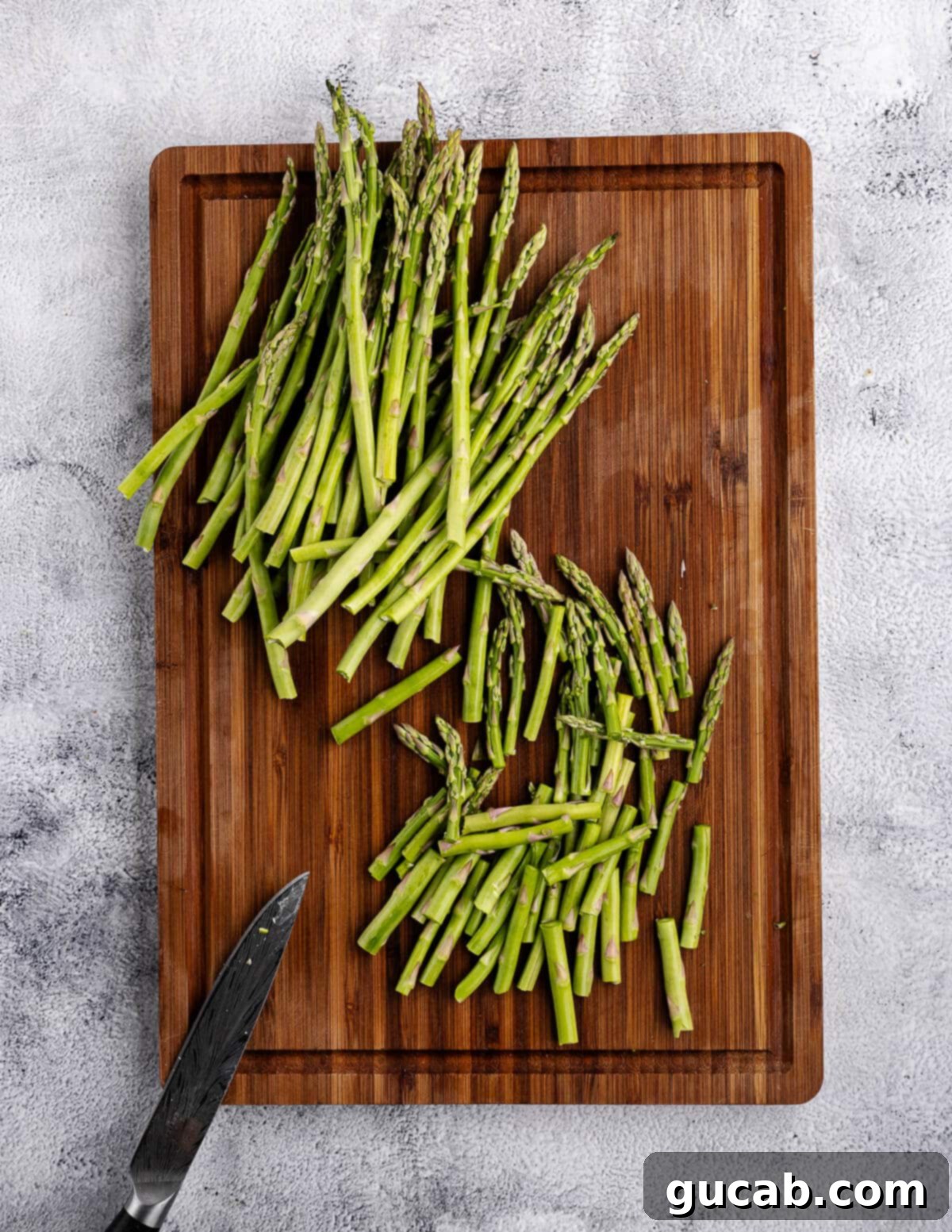 Fresh asparagus spears, trimmed and cut into uniform 2-inch pieces, arranged on a wooden cutting board.