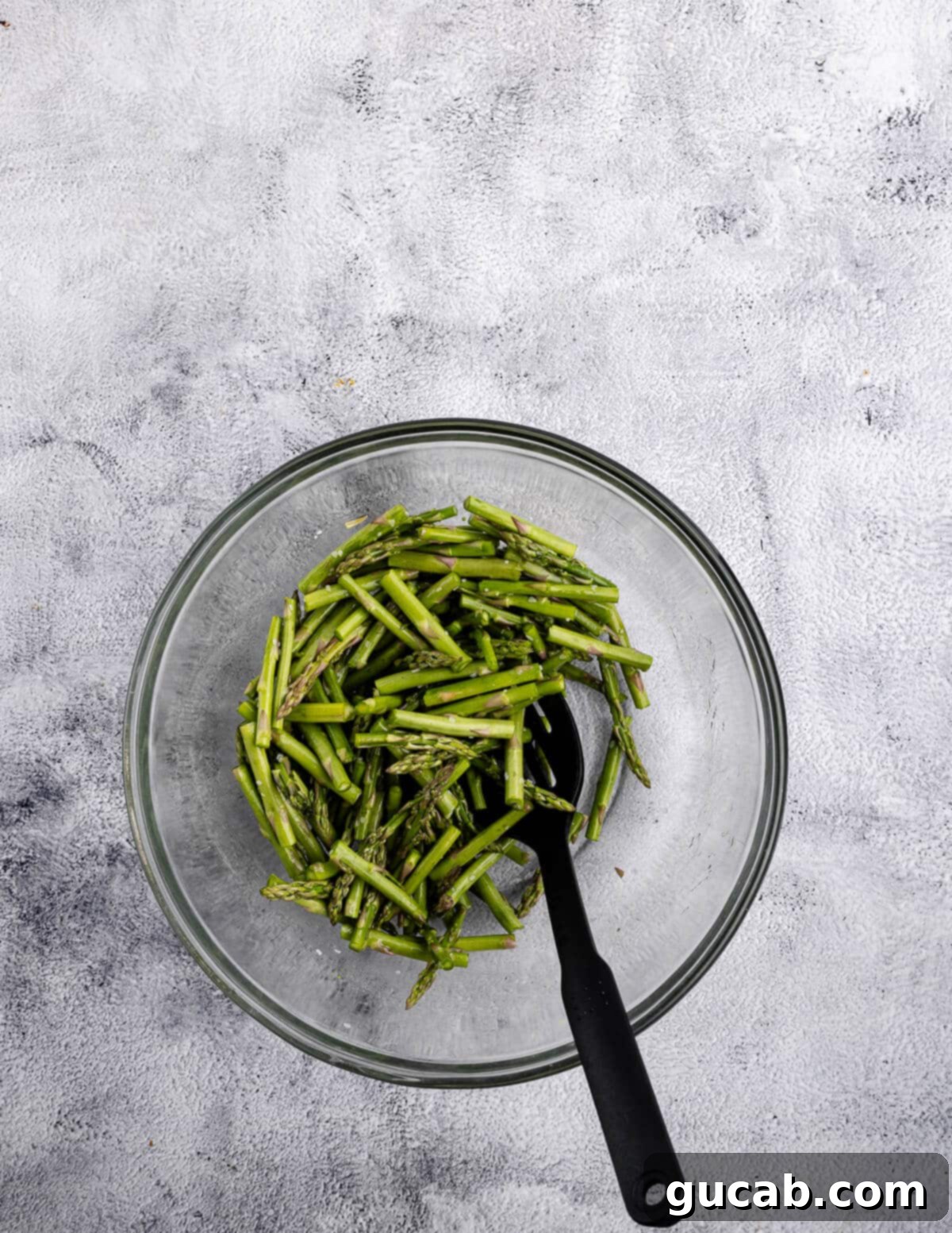 Cut asparagus pieces in a bowl, glistening with olive oil and salt, ready to be added to the roasted potatoes.