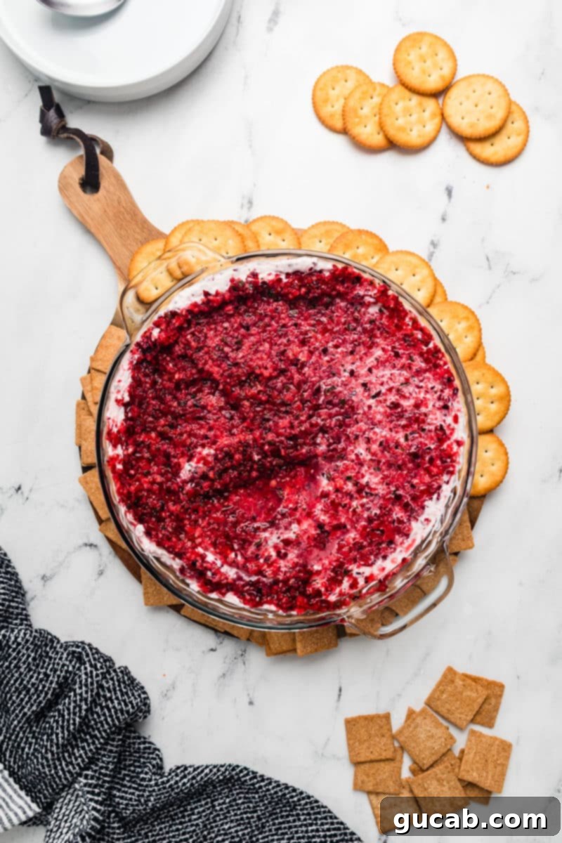 A vibrant cranberry jalapeno cream cheese dip in a white pie dish, surrounded by an array of butter crackers, ready to be served as a festive holiday appetizer.