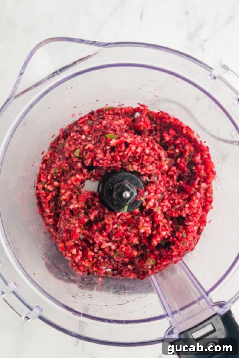 Coarsely chopped cranberry chutney mixture in a food processor bowl, showing the chunky texture of cranberries and jalapeno, ready for chilling.