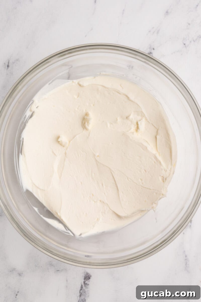 A large bowl filled with perfectly whipped cream cheese, showing its light, airy, and fluffy texture, ready for the next step of the dip preparation.