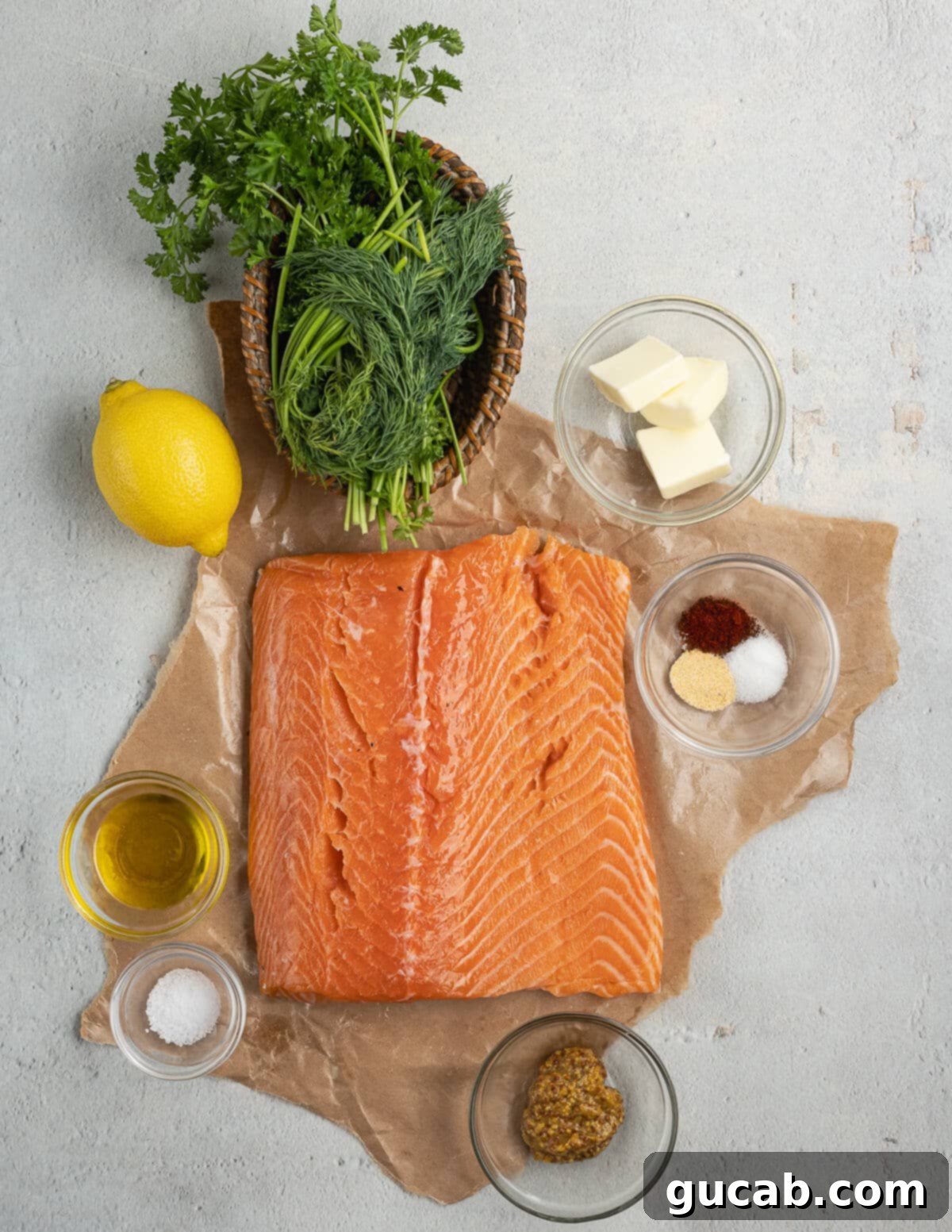 A colorful array of ingredients including fresh parsley, dill, a salmon fillet, butter, spices, a lemon, olive oil, and grainy mustard, all ready to be transformed into a flavorful dish.