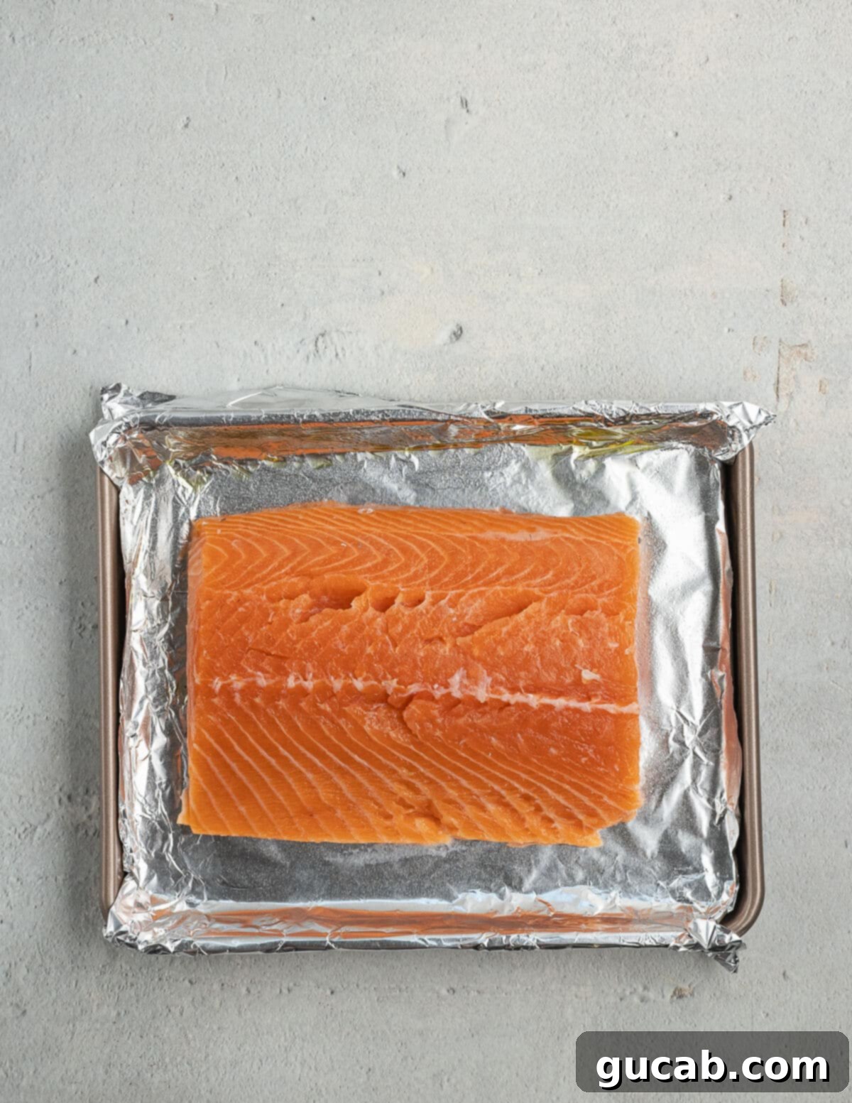 A fresh salmon fillet resting on an aluminum foil-lined toaster oven pan, ready to be seasoned and cooked to perfection.