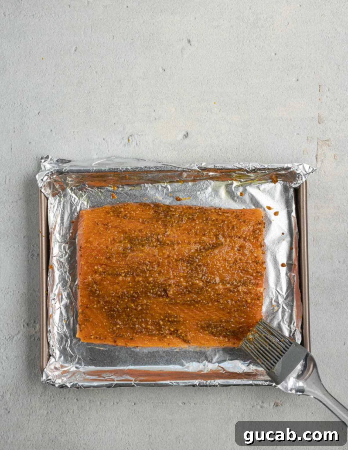 The salmon fillet is generously brushed with the spiced mustard mixture, ensuring that every part of the fish is coated in the flavorful marinade.