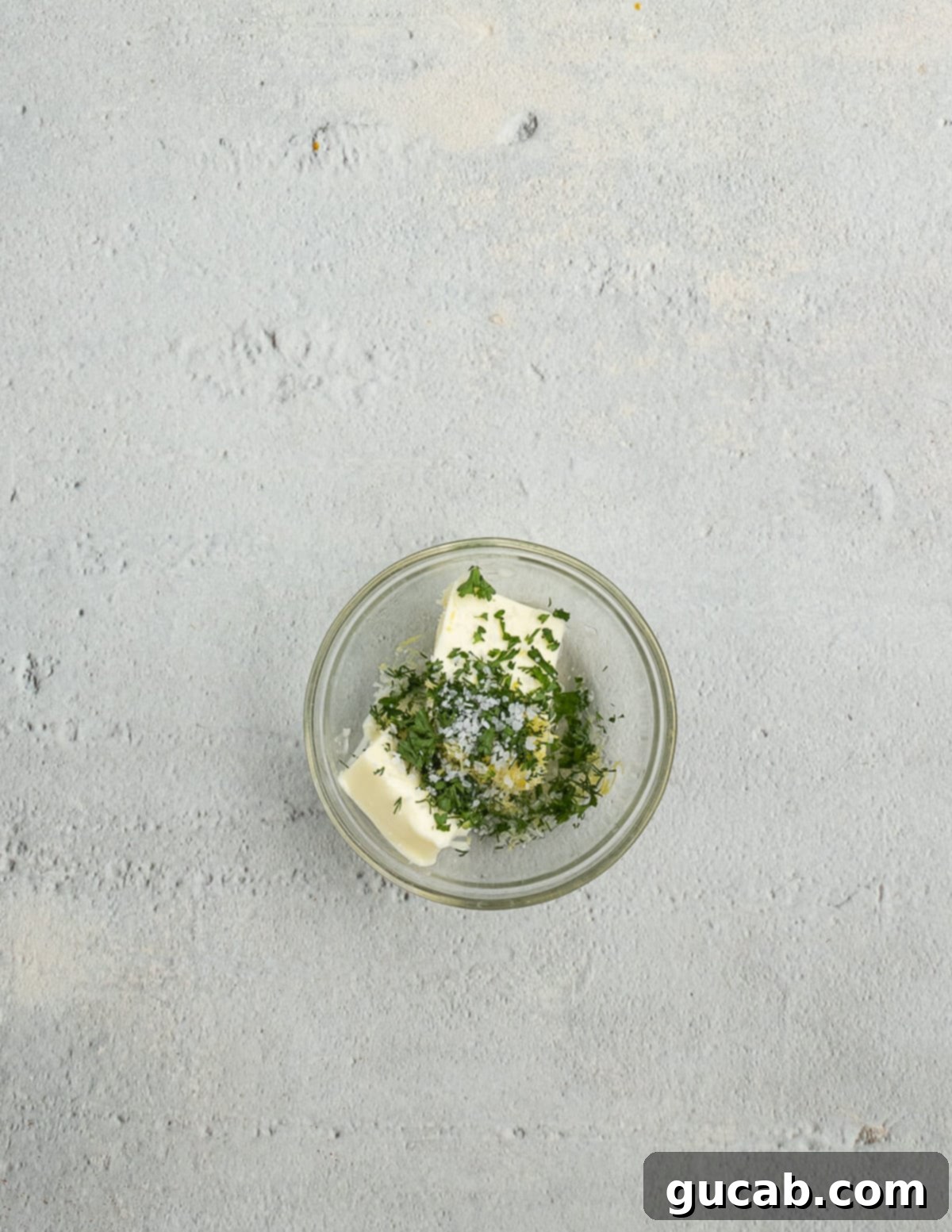 A bowl containing softened butter, fresh herbs, and a pinch of salt, ready to be mixed into a delectable herb butter.