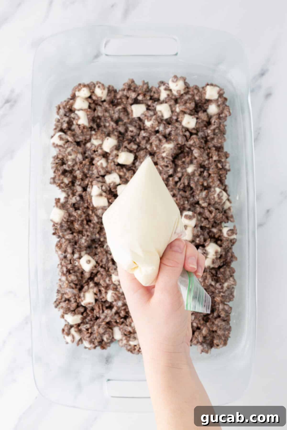 Hand holding a bag of melted white chocolate over Rice Krispie treats