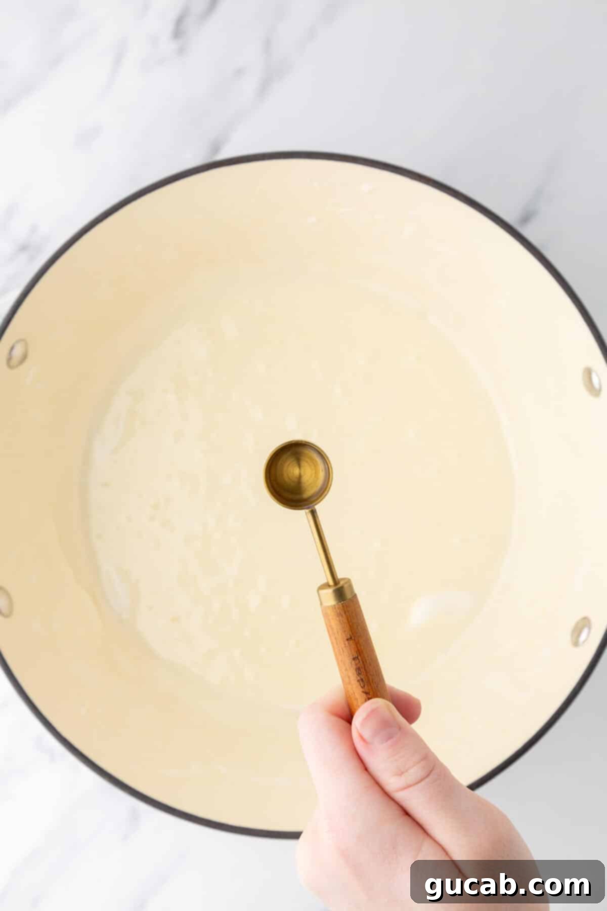 Melted butter and marshmallows in a Dutch oven with hand holding peppermint extract over top