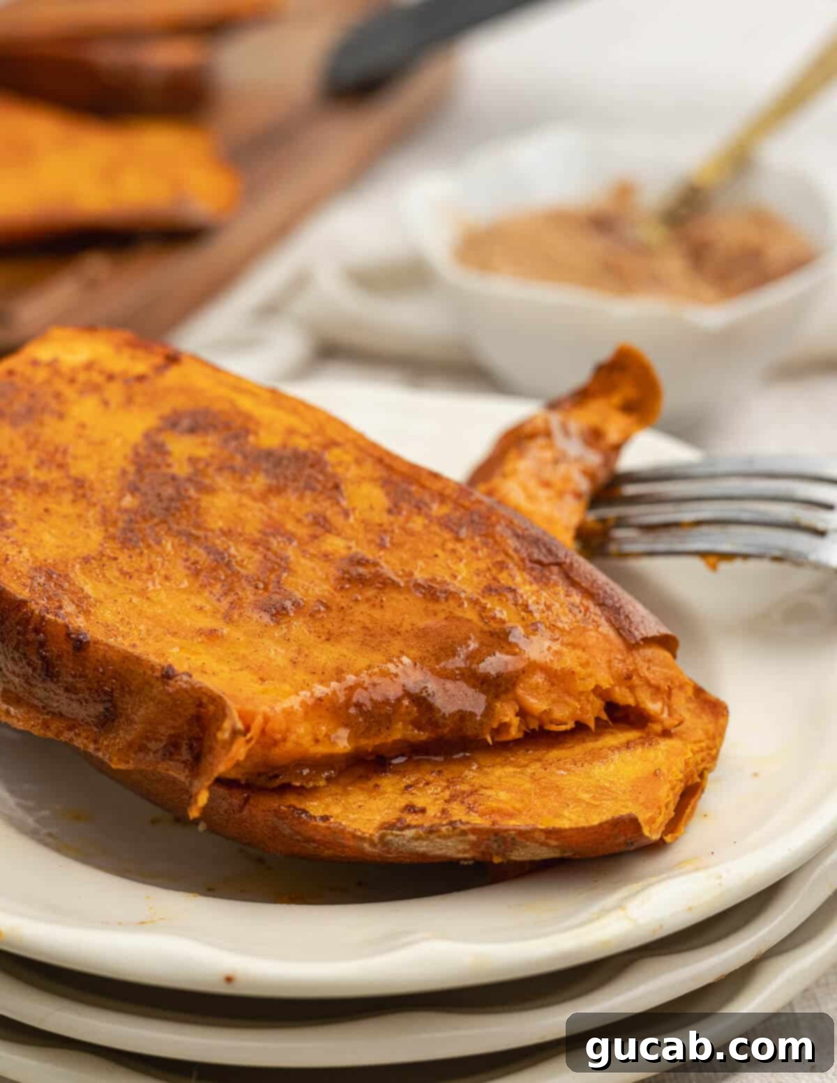 Perfectly baked sweet potatoes on a plate, drizzled with cinnamon maple butter that's melting slightly and creating a beautiful glaze.