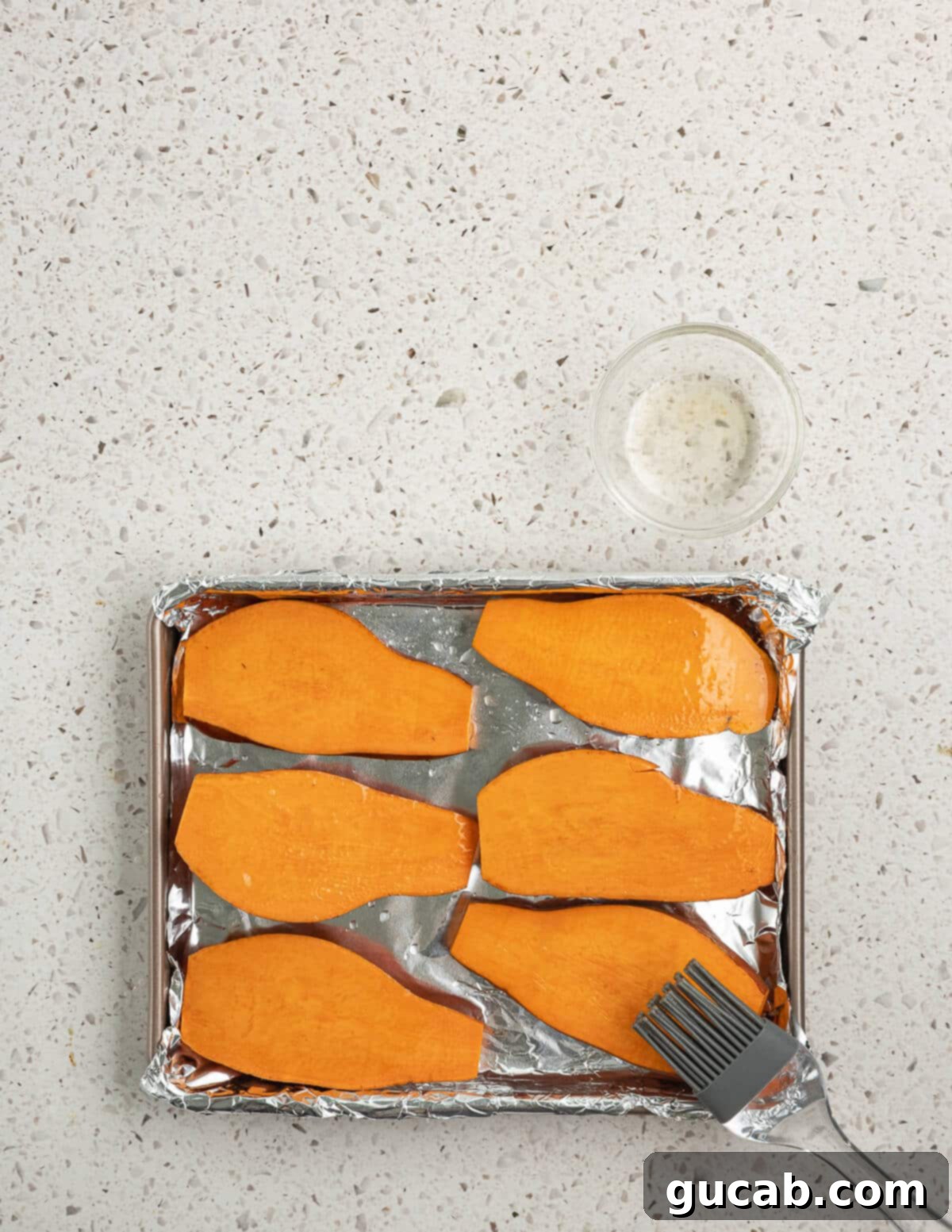 The sliced sweet potatoes are being brushed with oil on a sheet pan, ensuring they are evenly coated for optimal baking.