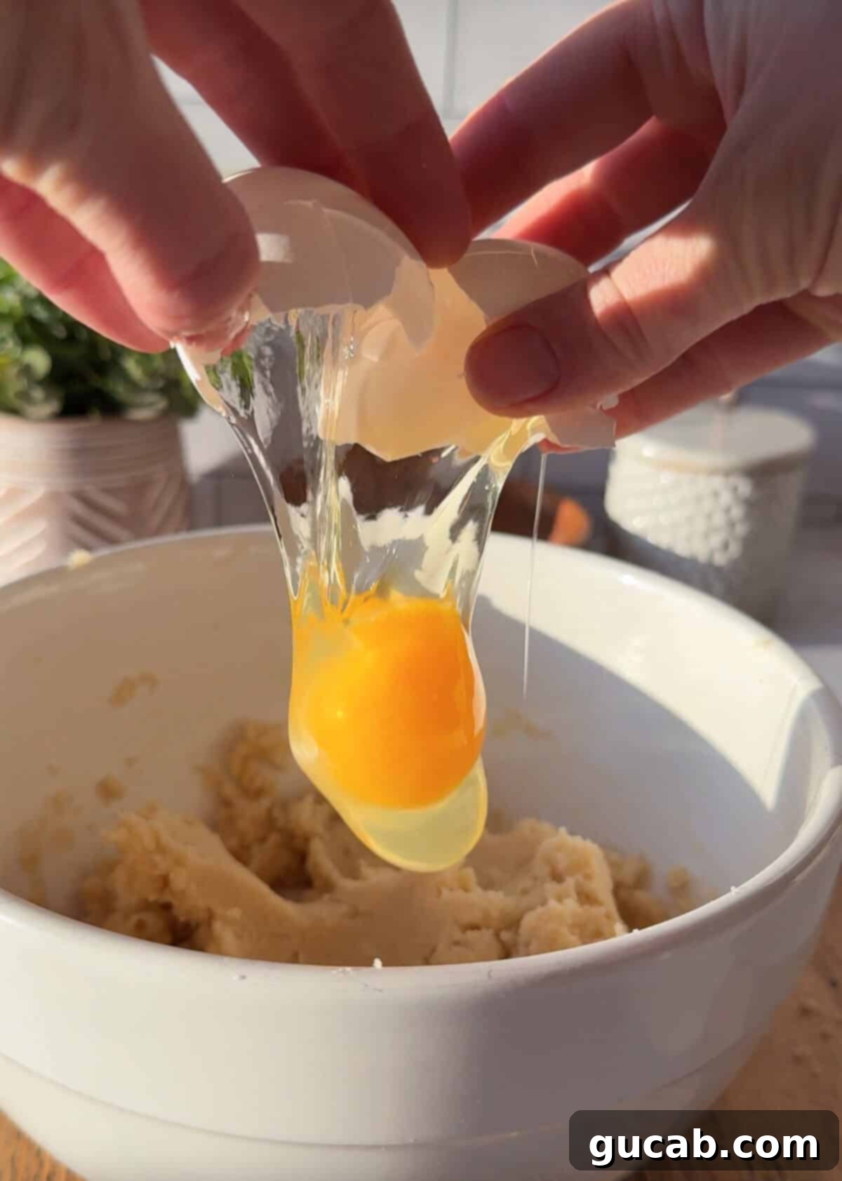 Oat Flour Double Chocolate Chunk Cookies 4 A hand carefully cracking an egg into a bowl of creamed butter and sugar, showing the initial stage of incorporating wet ingredients.