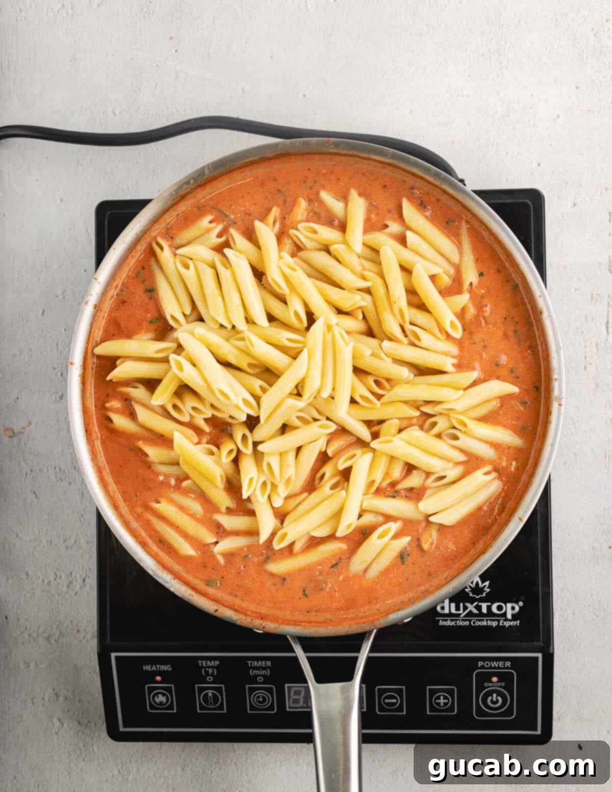 Penne pasta added to the vodka sauce in a skillet.