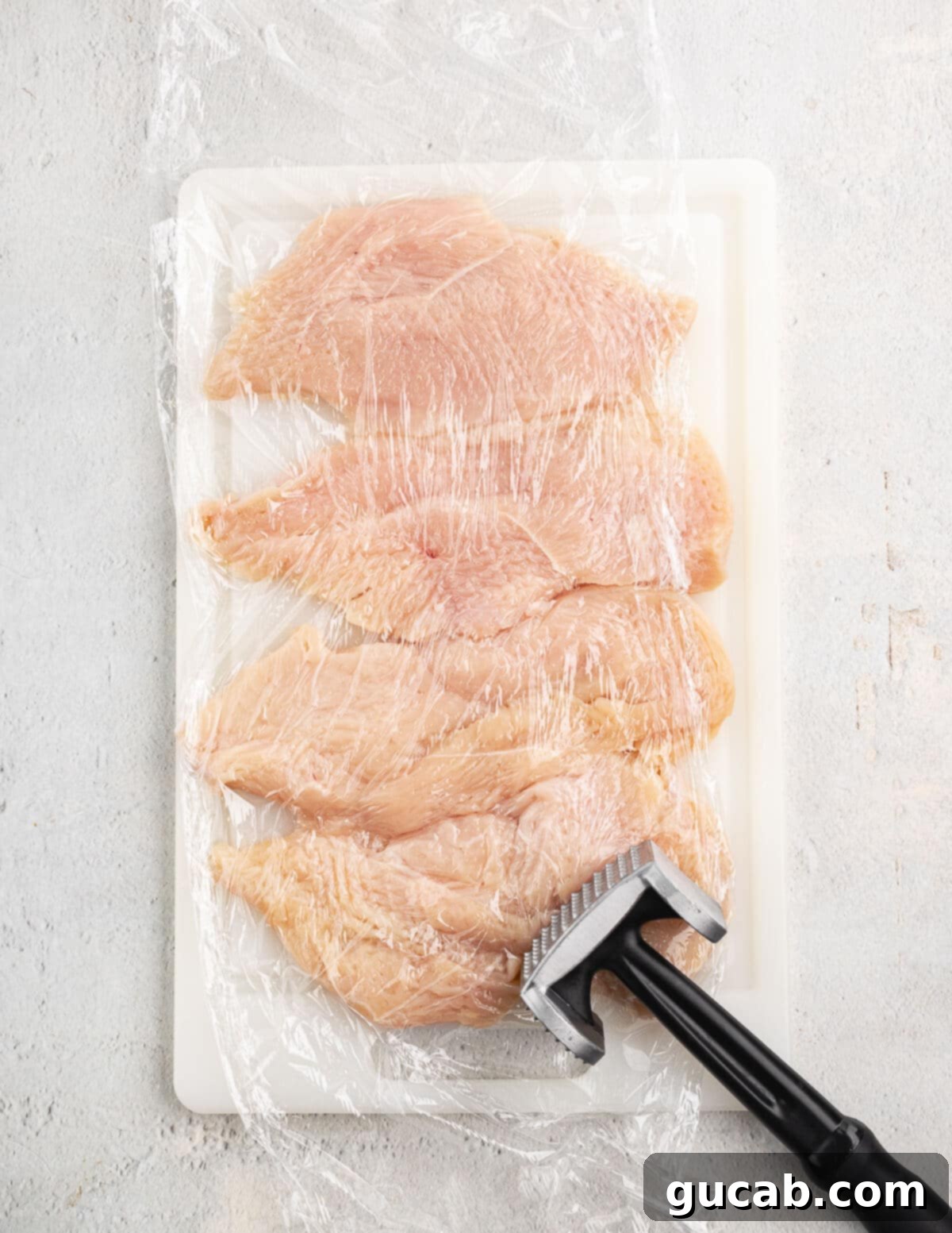 Pounded chicken breasts covered in plastic wrap.