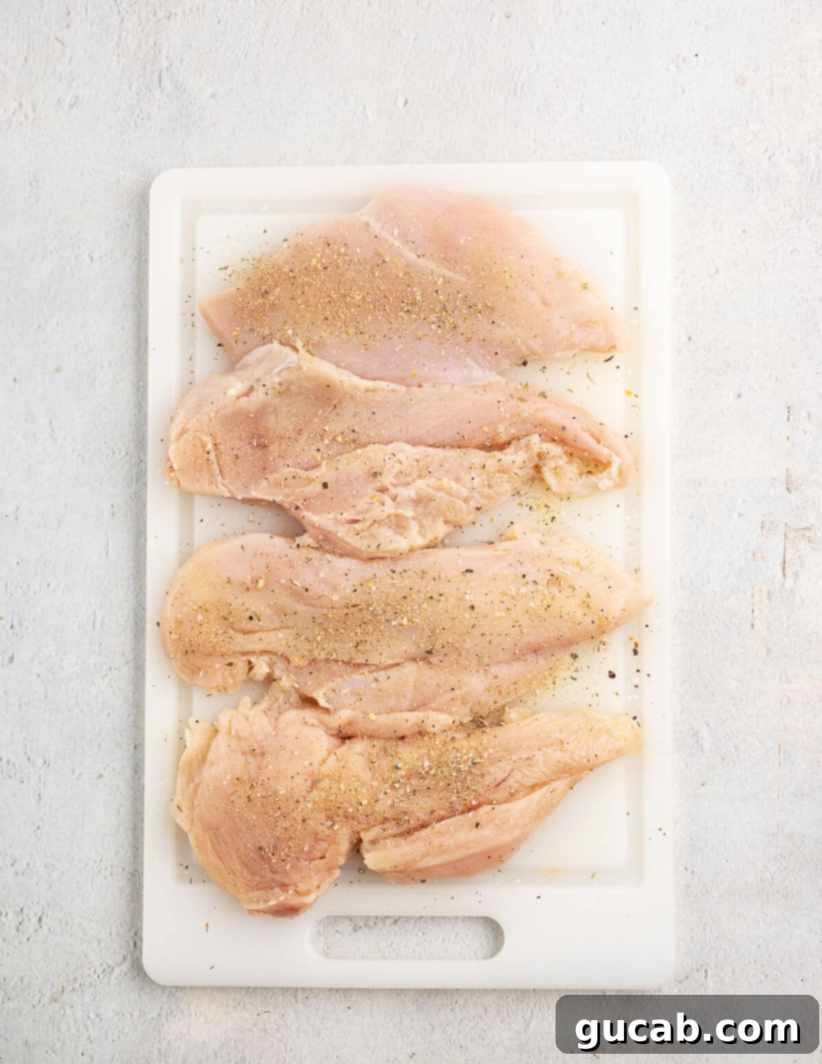 Pounded and seasoned chicken on a wooden cutting board.