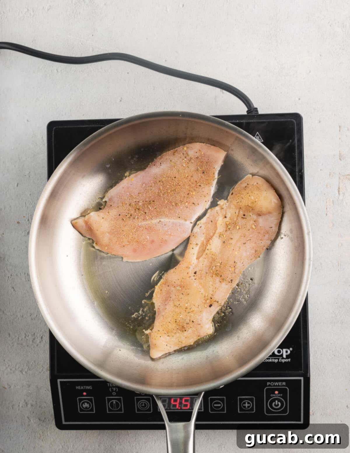 Raw, seasoned chicken in a skillet ready to be cooked.