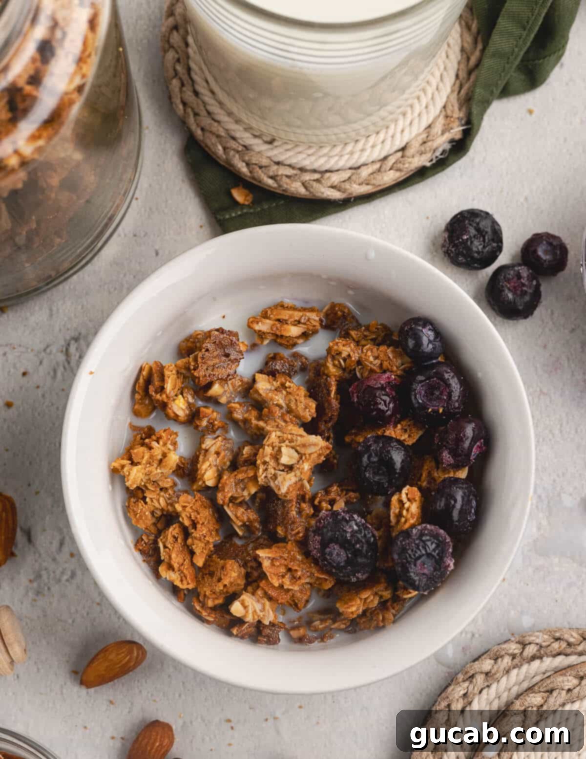 Almond Butter Crunch Granola 13 A bowl of almond butter granola served with fresh blueberries and milk, showcasing a delicious and healthy breakfast option