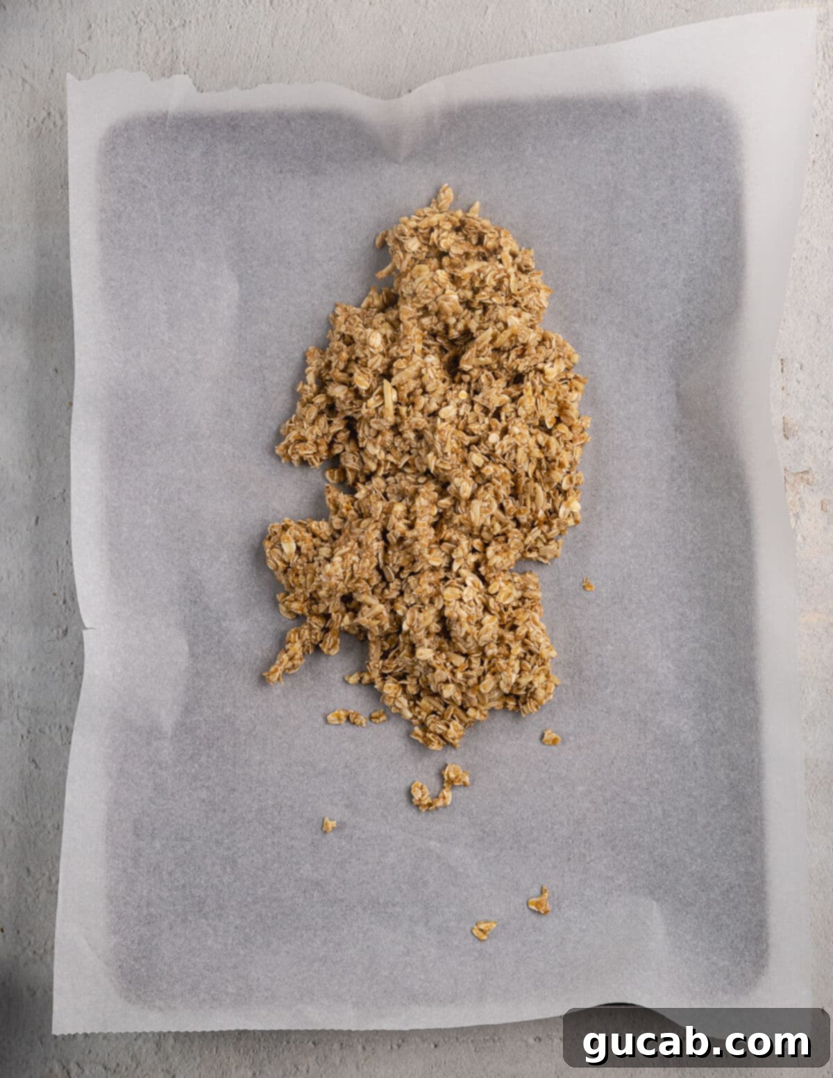 Almond Butter Crunch Granola 9 Granola mixture in a pile on a parchment-lined sheet pan, ready to be spread out for baking