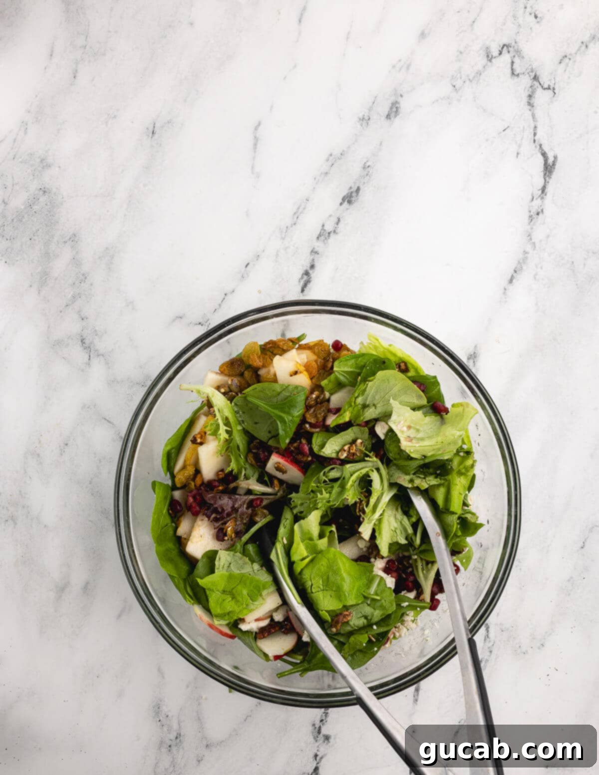 Pomegranate Pear Salad with Candied Pumpkin Seeds 11 Tongs tossing mixed greens with mix-ins.