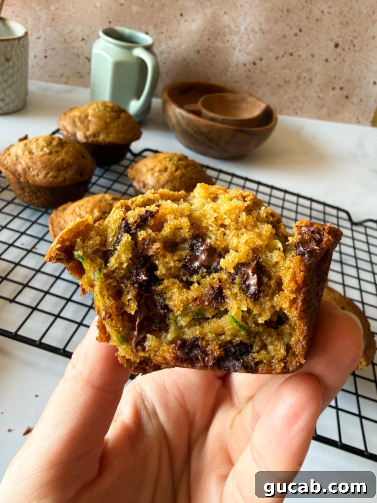 Heartwarming Zucchini Muffins 2 Hand holding half a zucchini muffin, showcasing its moist texture and deliciousness.