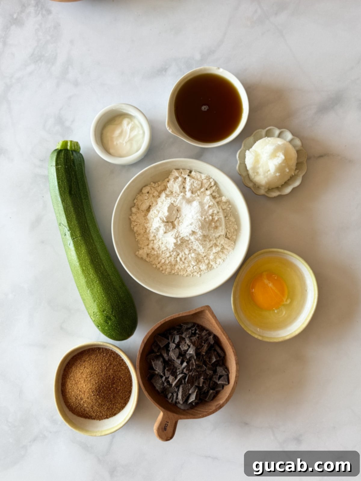 Heartwarming Zucchini Muffins 3 Arrangement of key ingredients: maple syrup, coconut oil, Greek yogurt, zucchini, egg, chocolate chips, coconut sugar, and gluten-free flour, beautifully showcasing the recipe's wholesome components.