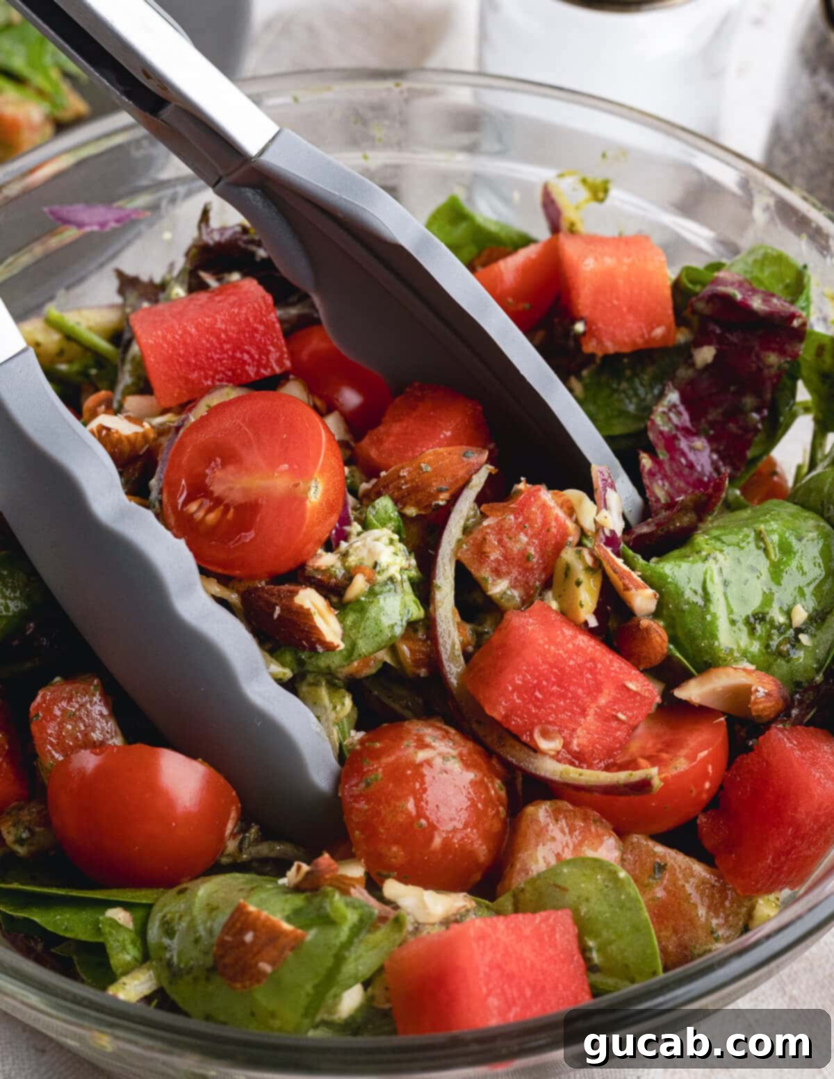 A visually appealing watermelon salad featuring watermelon, cherry tomatoes, red onion, roasted almonds, and goat cheese, dressed in a honey basil vinaigrette.