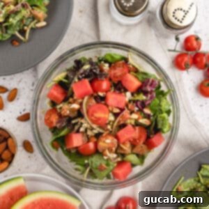 A beautifully plated watermelon salad with watermelon, greens, tomatoes, and goat cheese.