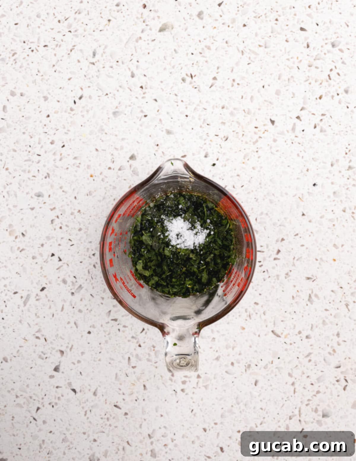 A clear glass cup containing olive oil, red wine vinegar, fresh basil, honey, and salt.