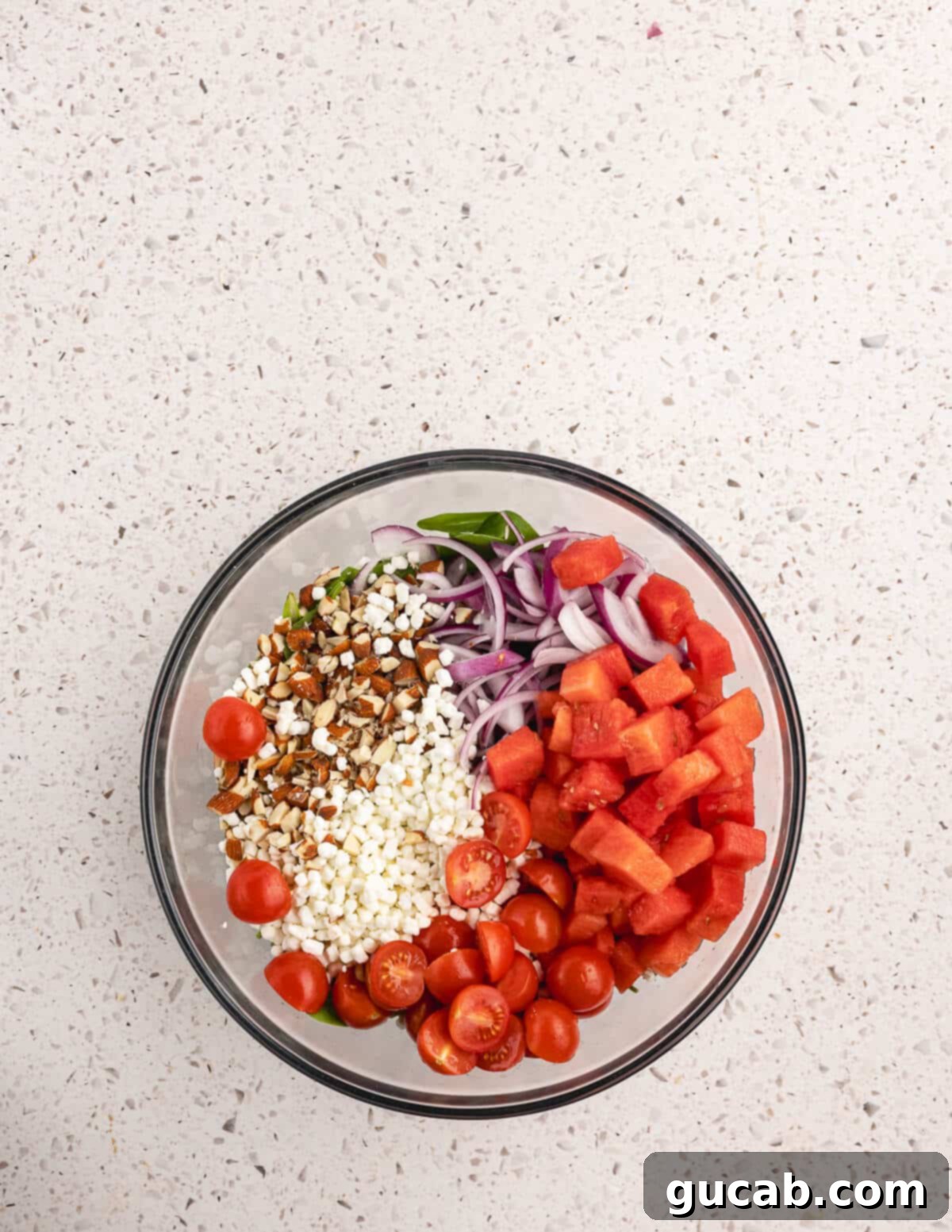 A colorful bowl brimming with mixed greens, watermelon, cherry tomatoes, goat cheese, almonds, and red onion.