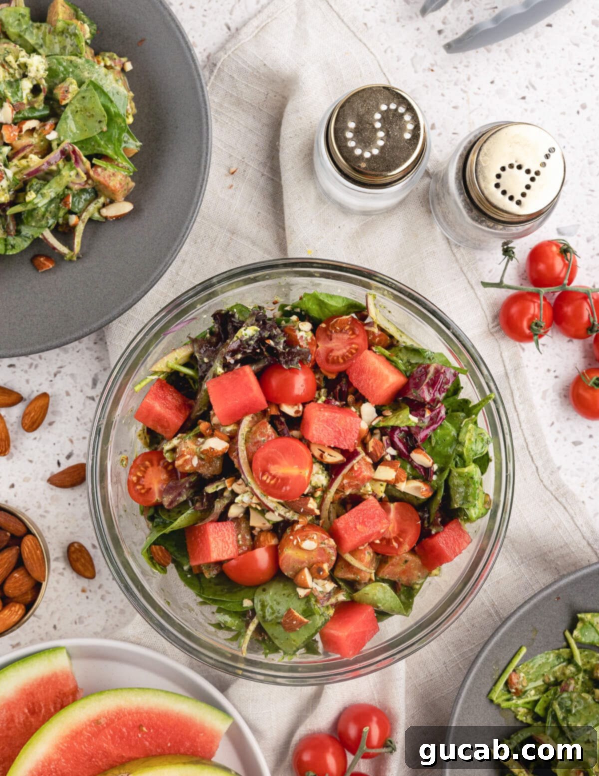 A vibrant and appetizing green salad with watermelon, tomatoes, red onions, almonds, and goat cheese.
